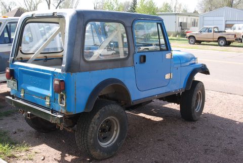 1981 Jeep CJ7 - A blue Jeep CJ7 with a hardtop is parked on a gravel lot next to a white truck.