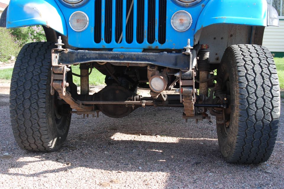 Blue Jeep CJ7 front axle, leaf springs, and tires. Visible rust on suspension components