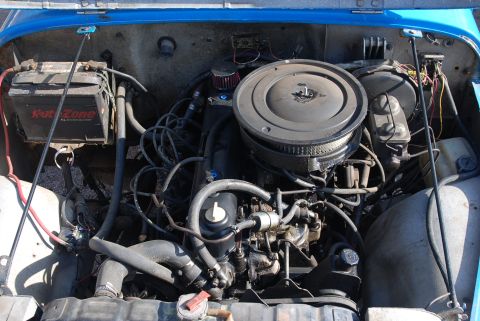 1981 Jeep CJ7 - The engine compartment of a blue Jeep shows the battery, hoses, and engine components.