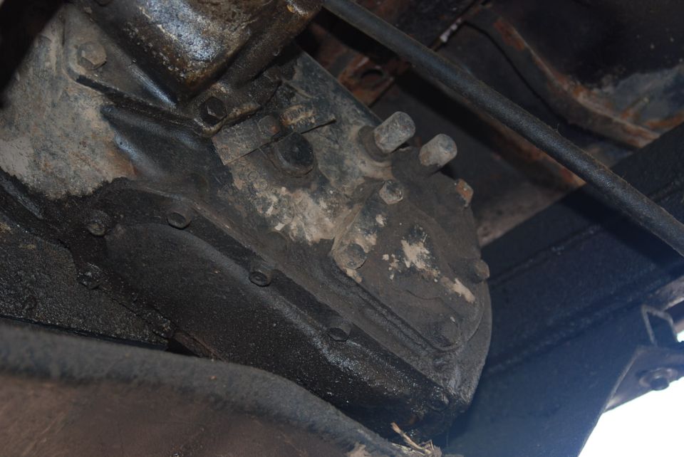 Close-up of a greasy, bolted metal component, likely part of a vehicle's transmission or drivetrain