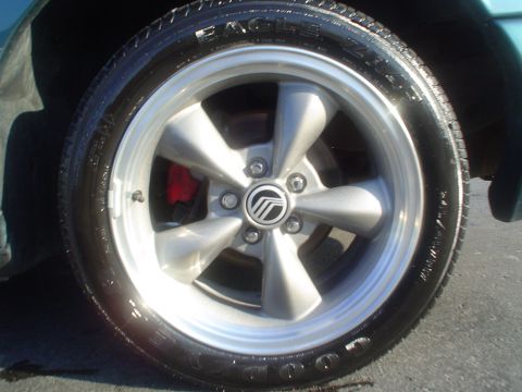 1996 Mercury Grand Marquis - A close-up view of a car's wheel, showing the Mercury logo on the hubcap and a red brake caliper.