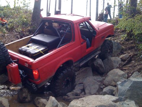 1989 Ford Bronco - Red 1989 Ford Bronco with roll cage and off-road tires navigating a rocky trail.