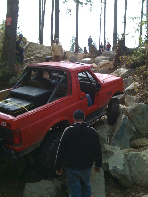 1989 Ford Bronco - A red SUV with a roll cage is shown off-roading over large rocks.