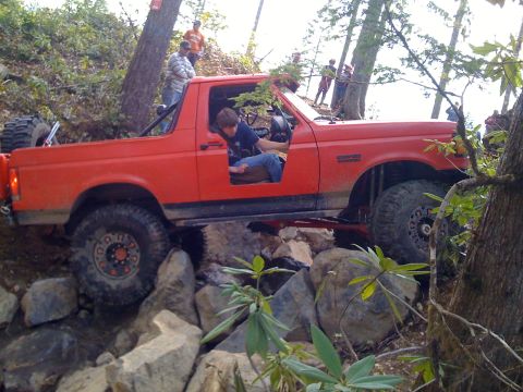 1989 Ford Bronco - A red Ford Bronco navigates a rocky trail with a person in the driver's seat.