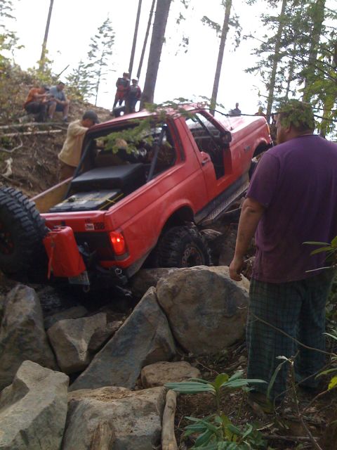 1989 Ford Bronco - A red 1989 Ford Bronco is shown navigating a challenging rocky terrain with several people observing.