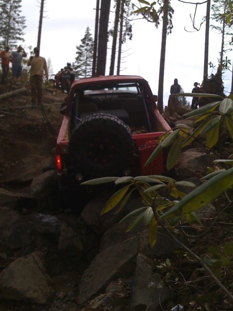 1989 Ford Bronco - A red pickup truck is shown off-roading on a rocky trail with several people observing the action.