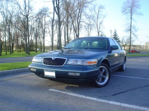 1996 Mercury Grand Marquis - A dark green sedan is parked in a lot with trees in the background.