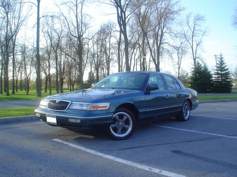 1996 Mercury Grand Marquis - A 1996 Mercury Grand Marquis is parked in a lot with trees in the background.