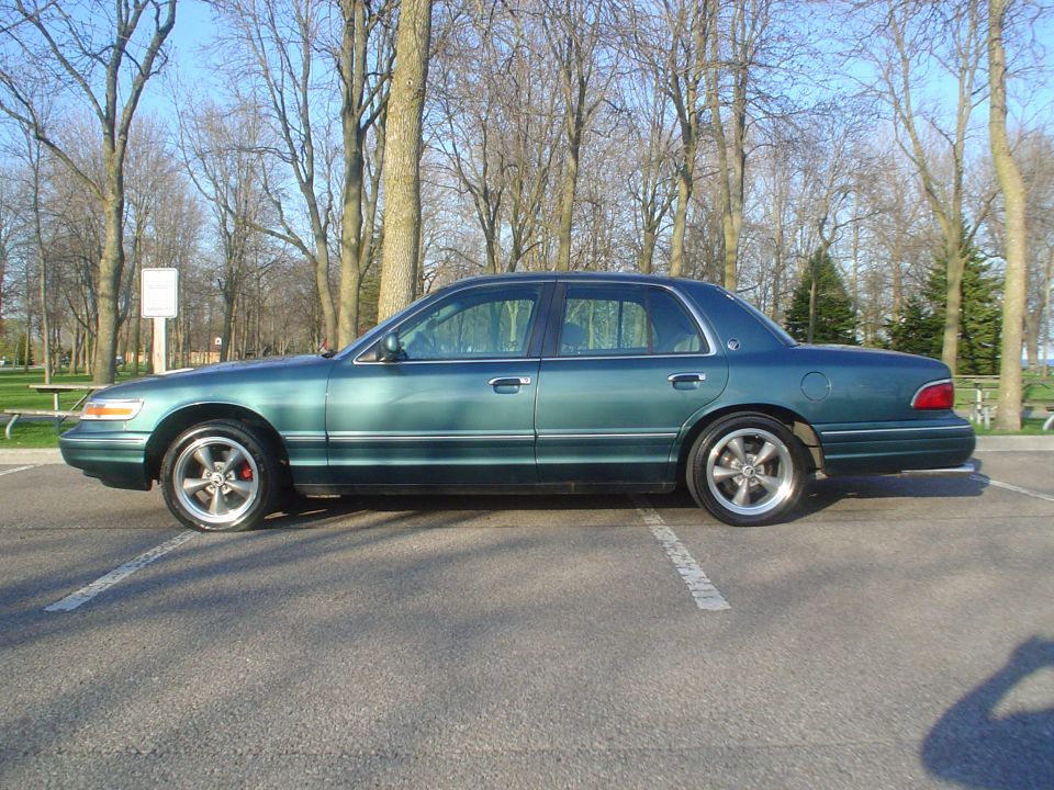 Side view of a green sedan with aftermarket wheels parked in a lot
