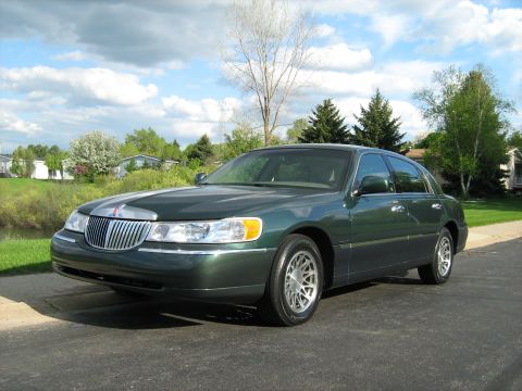 1988 Mercury Grand Marquis - A dark green sedan is parked on a paved surface with a suburban background under a cloudy sky.