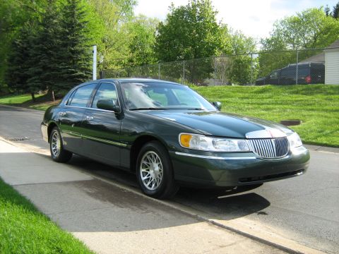 1988 Mercury Grand Marquis - A dark green Lincoln Town Car is parked curbside on a sunny day with trees and a fence in the background.