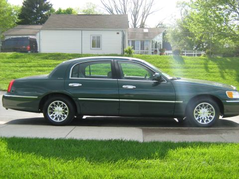 1988 Mercury Grand Marquis - A side view of a dark green 2001 Lincoln Town Car sedan is shown parked in front of a residential house.