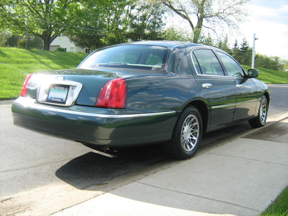 Dark green sedan parked on a concrete driveway, rear view. Chrome trim around license plate and taillights