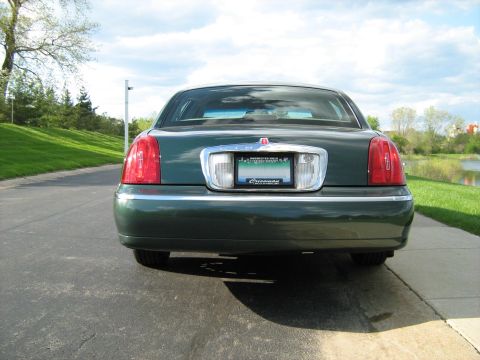 1988 Mercury Grand Marquis - The rear of a dark green sedan is shown parked on a paved surface with a grassy embankment and a lake in the background.