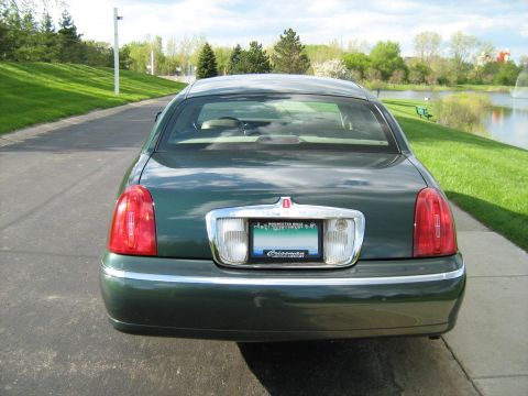 1988 Mercury Grand Marquis - Rear view of a green sedan parked on a paved surface next to a grassy area and a lake.