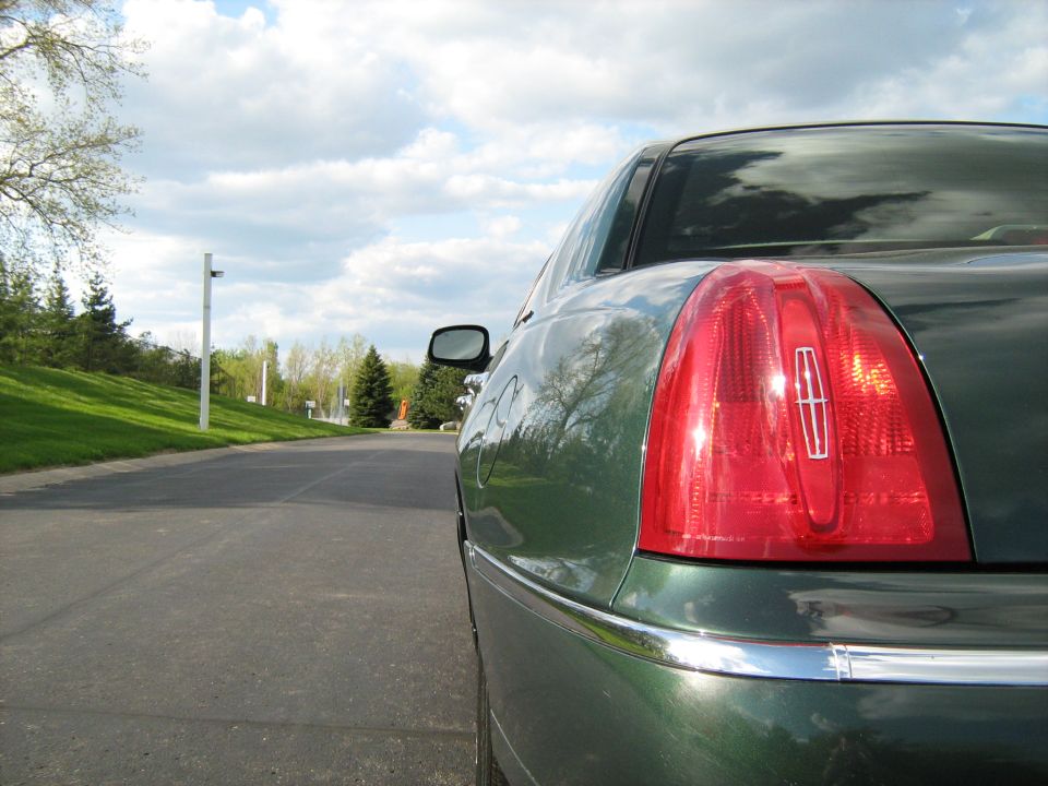 Rear quarter panel and taillight of a green sedan parked on a road