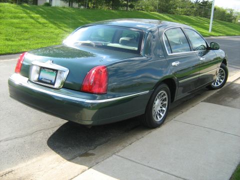 1988 Mercury Grand Marquis - A dark green sedan is parked on the side of the road, with a grassy hill in the background.