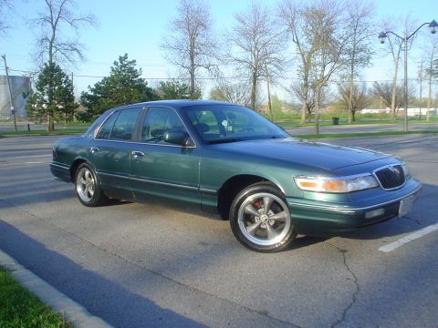 1996 Mercury Grand Marquis - Green 1996 Mercury Grand Marquis with custom wheels sits in a parking lot under a clear sky.