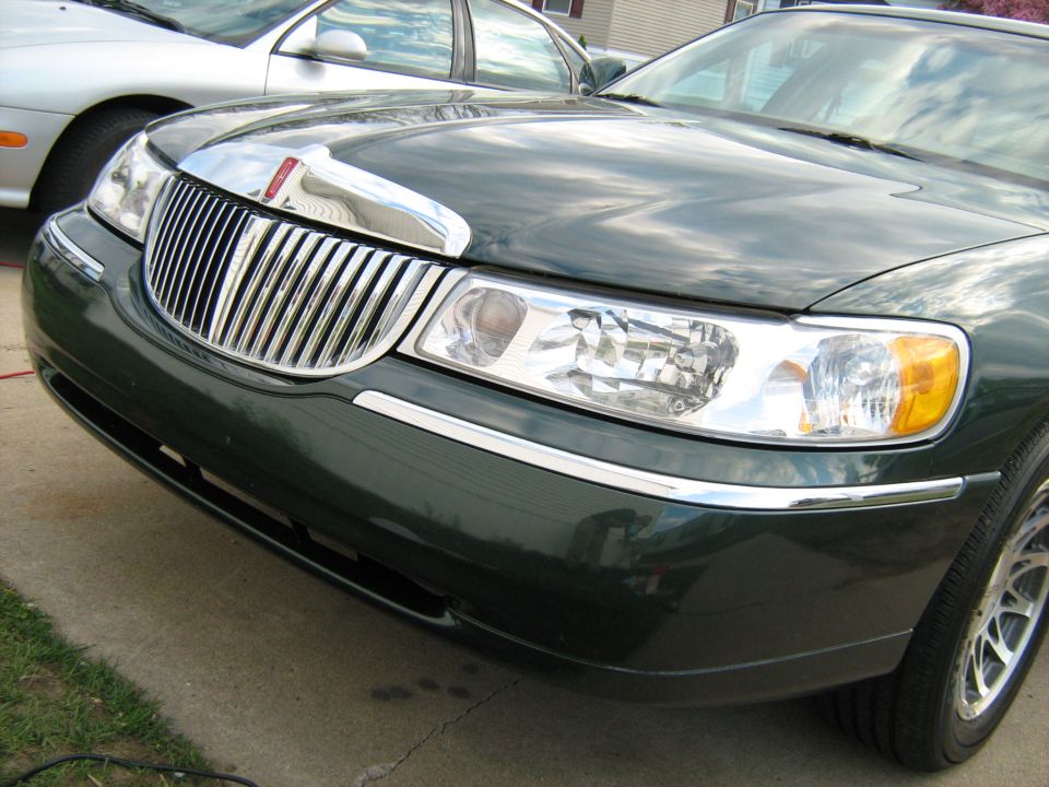 Green Lincoln Town Car front grille and headlights, chrome trim, parked on concrete