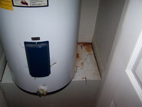 1978 Ford Bronco - A white water heater with a blue access panel and a yellow warning label is shown, with signs of water damage on the floor.