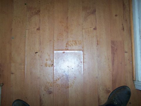 1978 Ford Bronco - A view of a wooden floor with water stains and a square metal plate, with feet visible at the bottom.