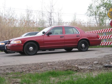 2000 Ford Crown Victoria - Two sedans are parked side-by-side on a dirt road, with a striped barrier in the background.