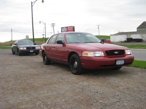 2000 Ford Crown Victoria - Two Ford Crown Victorias are parked on a gravel lot under an overcast sky.
