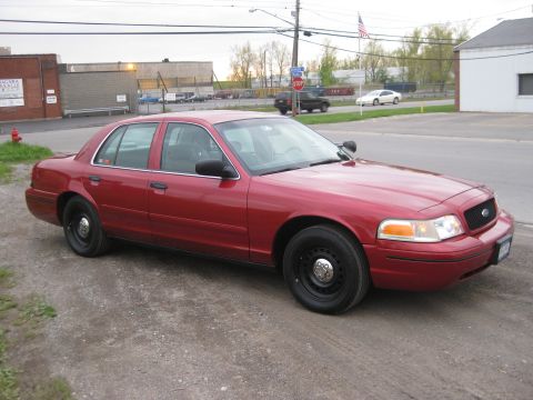 2000 Ford Crown Victoria - This red 2000 Ford Crown Victoria sedan is shown from the front quarter angle, parked on a gravel surface.