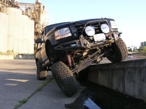 1996 Ford Bronco - This modified pickup truck is shown with its front tire on a concrete barrier, demonstrating its off-road capabilities.