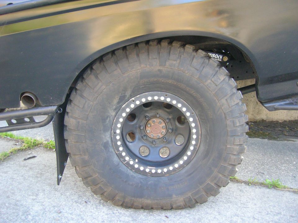1996 Ford Bronco rear wheel with large off-road tire, custom beadlock wheel, and fender flare. Exhaust pipe visible