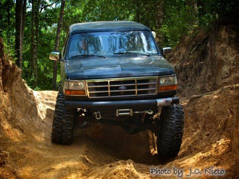 1995 Ford Bronco - A dark SUV navigates a challenging dirt path through a wooded area.