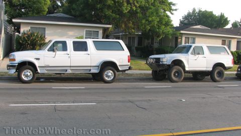 1996 Ford C-350 (Centurion Conversions) - Two white Ford SUVs are parked on a residential street.