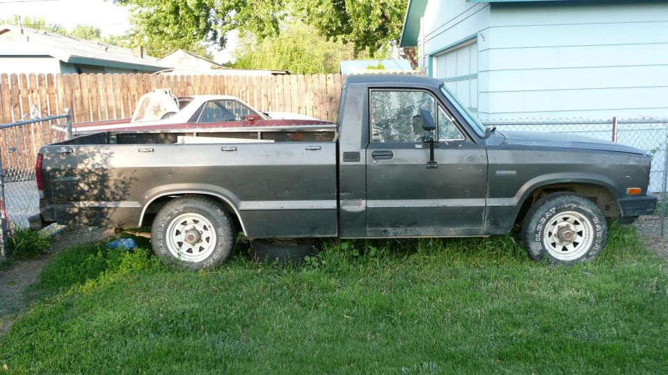 Dark gray pickup truck with a red car in the bed, parked on grass