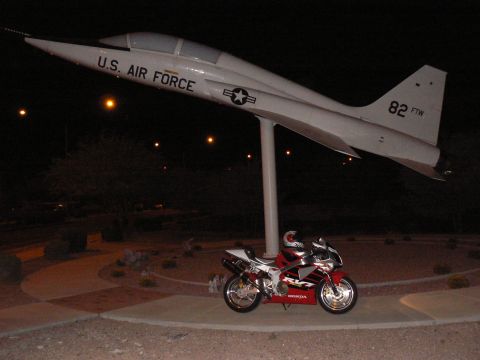 1978 Ford Bronco - A Honda motorcycle is parked beneath a static display of a U.S. Air Force jet at night.