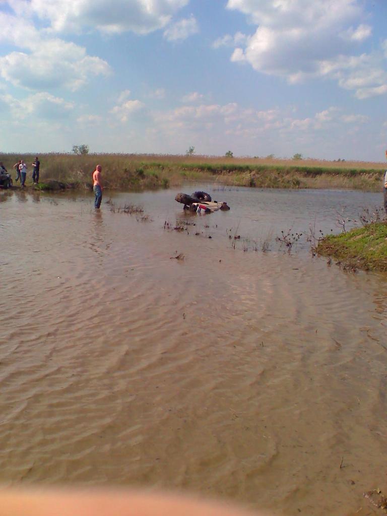 off-road vehicle submerged in shallow water with people standing nearby