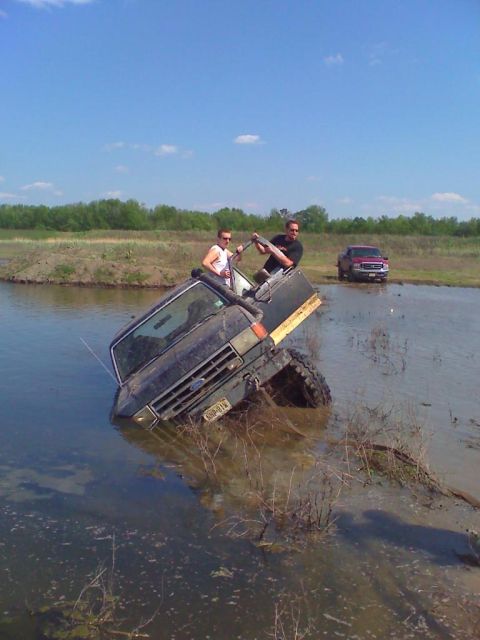 1990 Ford Bronco - A 1990 Ford Bronco is stuck in the water with two occupants, while another truck is visible in the background.