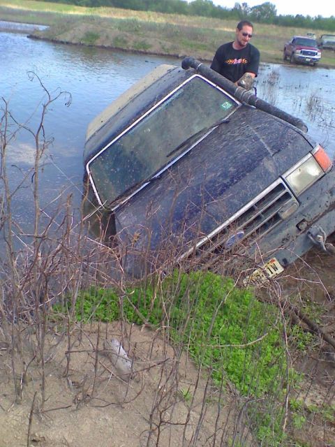 1990 Ford Bronco - A 1990 Ford Bronco is stuck in a body of water, with a man observing the situation.