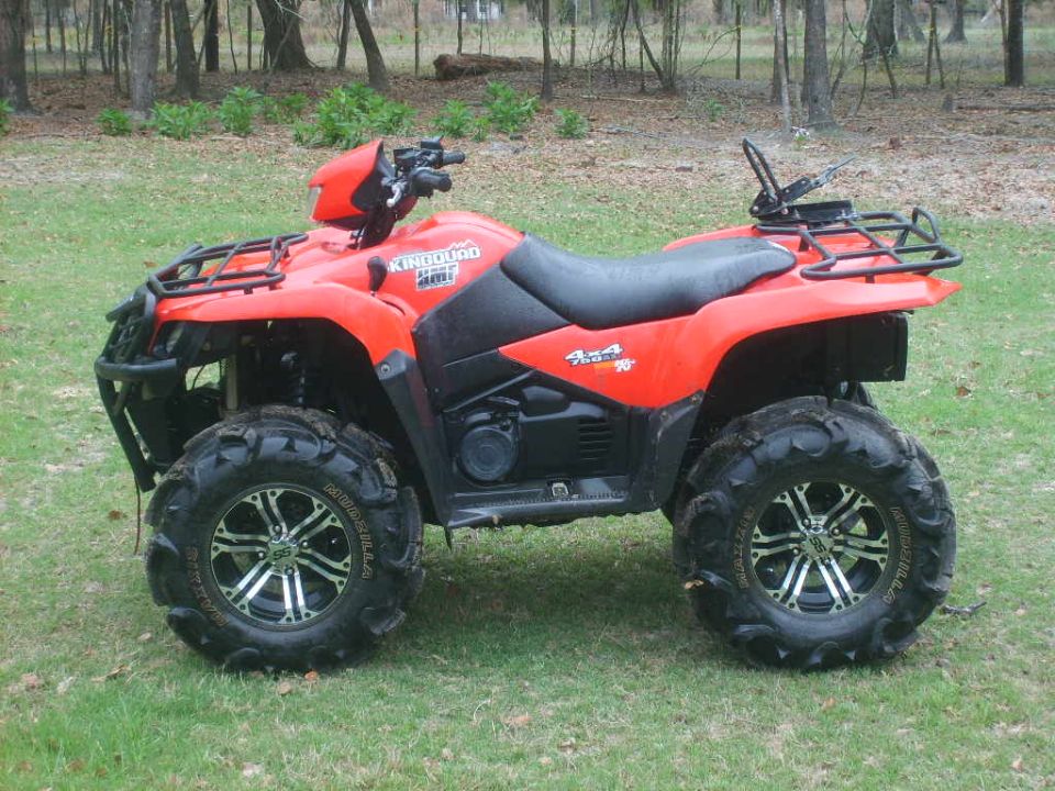 Red Suzuki King Quad ATV, side view, on grass with mud tires and alloy wheels.