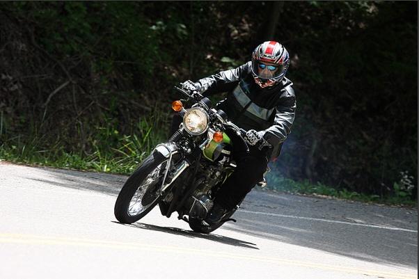 Motorcyclist in helmet and leather jacket leaning into a turn on a road with trees