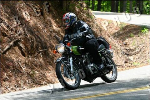 1985 Ford LTD Crown Victoria - A rider on a green Honda motorcycle navigates a curve on a tree-lined road.