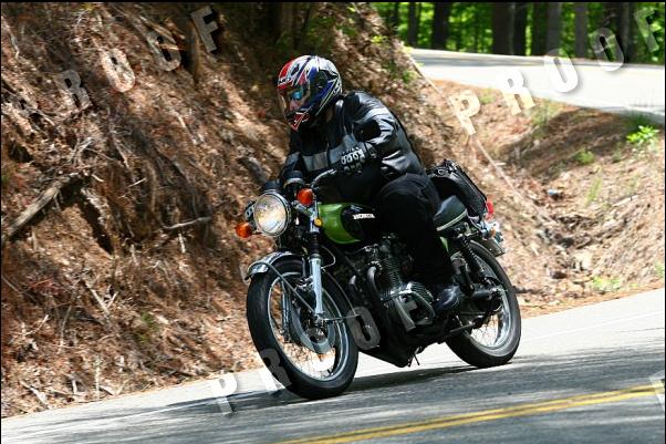 Green Honda motorcycle with a rider in a black leather jacket and helmet on a winding road