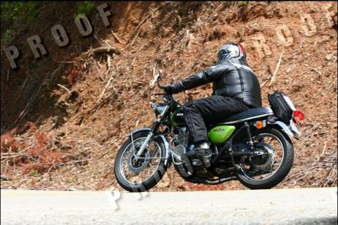 1985 Ford LTD Crown Victoria - A rider on a green motorcycle navigates a scenic road, with a wooded hillside in the background.