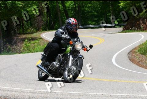 1985 Ford LTD Crown Victoria - A motorcyclist navigates a sharp curve on a tree-lined road.