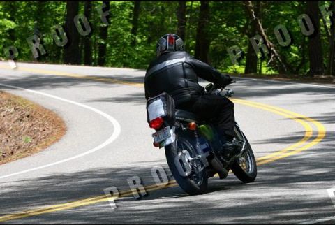 1985 Ford LTD Crown Victoria - Rider on a motorcycle navigates a curve on a tree-lined road.