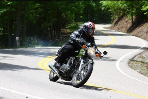 1985 Ford LTD Crown Victoria - A motorcycle rider navigates a curved road surrounded by trees.