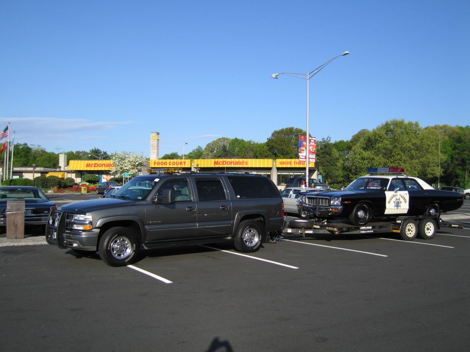Gray Suburban with trailer hauling a police car in a McDonald's parking lot