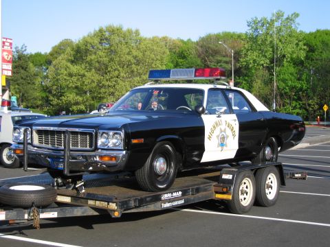 1991 Ford LTD Crown Victoria - Front three-quarter view of a black-and-white Highway Patrol sedan loaded on a flatbed trailer with a spare tire alongside.