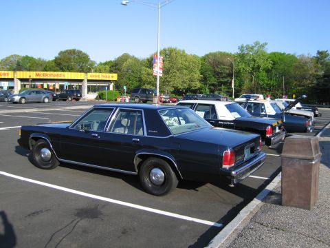 1991 Ford LTD Crown Victoria - dark-blue four-door sedan parked in a lot alongside several marked patrol cars in front of a McDonald's.