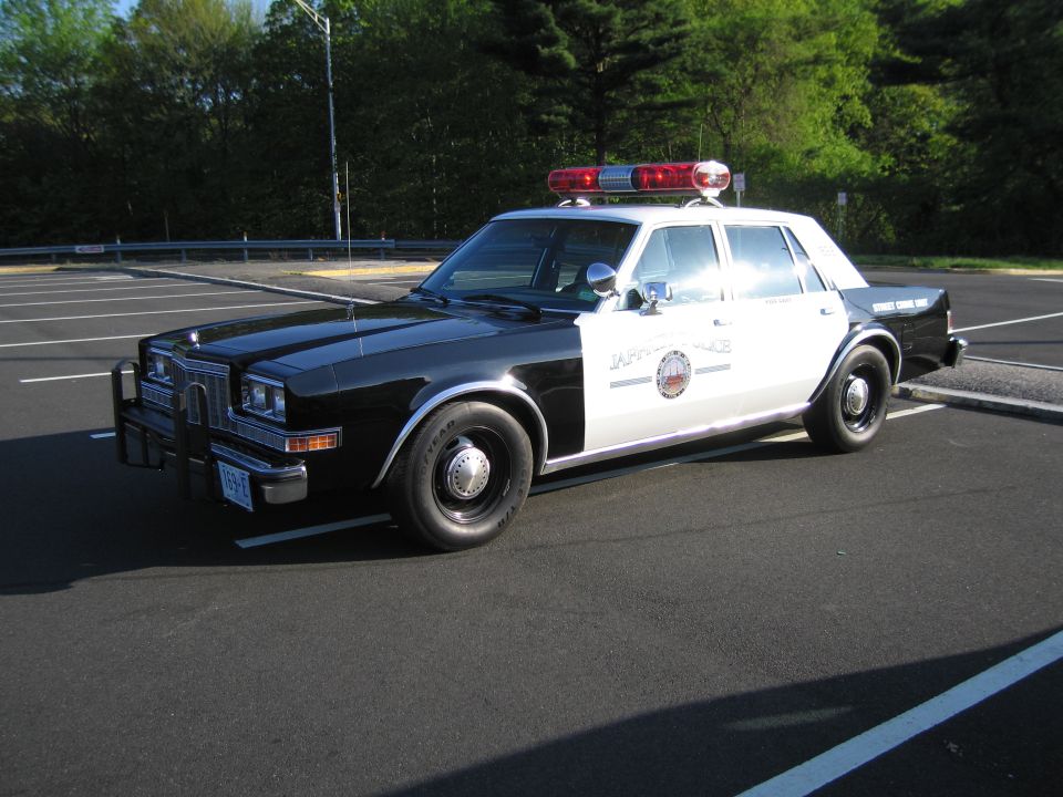 Black and white police sedan with red lightbar parked in an empty lot