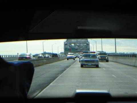1991 Ford LTD Crown Victoria - Through a car windshield, a convoy of police cruisers with light bars drives along a highway toward a bridge structure.